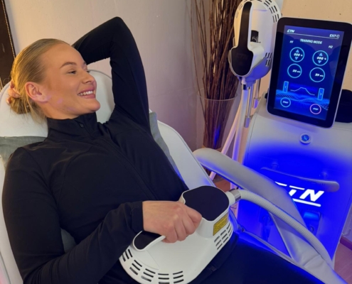 Nainen X-Tone lihasstimulaatiolaitteessa saa hoitoa vatsalihaksiin yhdellä hoitokahvalla.